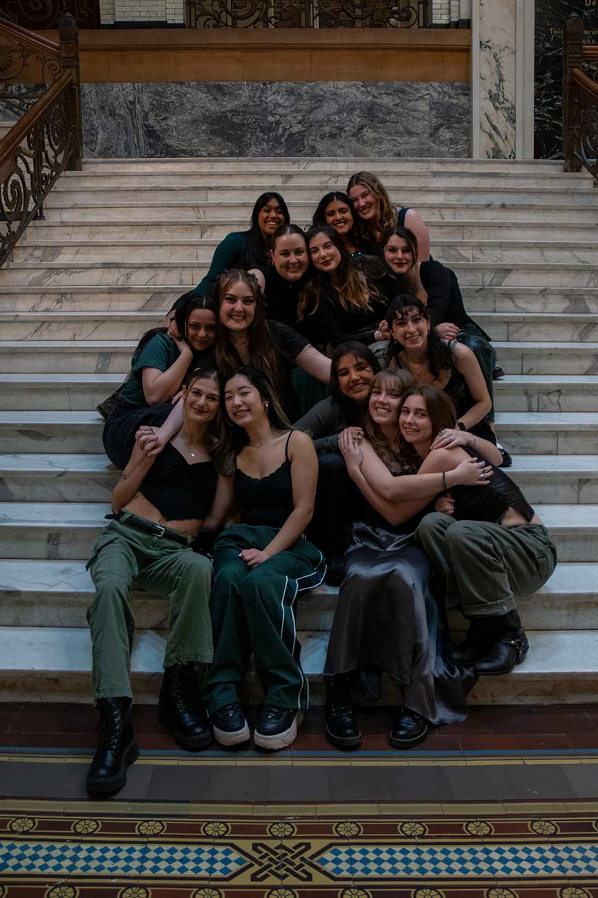 Drexel University Treblemakers acapella group girls sitting on marble stairs huggin and smiling