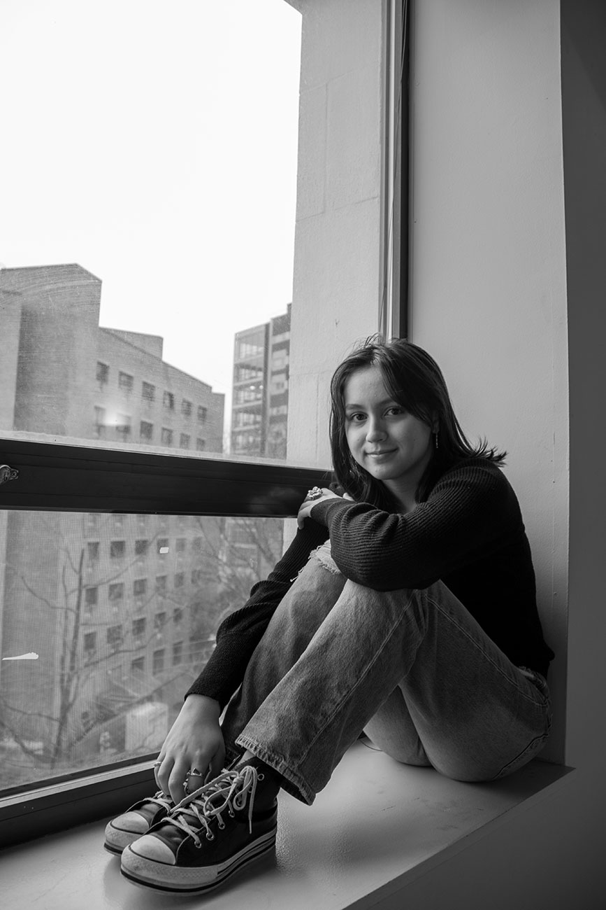 Black and white, girl sitting, leaning on knees on window ledge corner